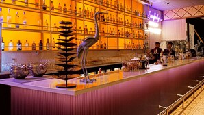A bar area with a long counter, shelves with bottles, and a decorative bird sculpture. - Just B Boutique Hotel (Vagator)