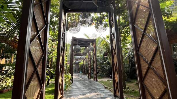 A pathway with hexagonal tiles leading through a structure with metal mesh walls and hanging spherical light fixtures. - Just B Boutique Hotel (Vagator)