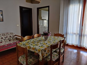 Een eethoek met een tafel voor vier personen, stoelen, een bloemenbank en een keuken op de achtergrond.