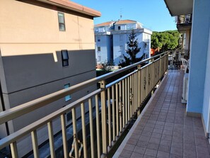 A balcony with a metal railing, a tiled floor, and buildings in the background.