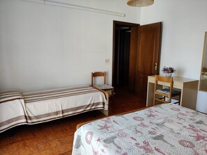 Un dormitorio con dos camas individuales, un escritorio de madera con una silla, un espejo y una puerta que da a otra habitación.