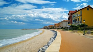 A coastal walkway with pebbles, a sandy beach, and buildings with balconies. - Spacious Apartment Close to the Beach (Caorle)