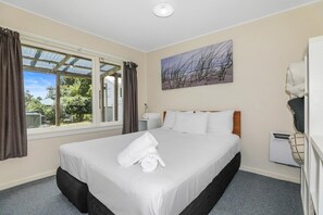 A hotel room with a bed, a window with curtains, a painting on the wall, and a white radiator.