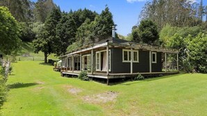 Une maison de plain-pied avec un porche, entourée d’une cour verdoyante et d’arbres.