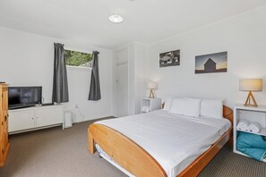 A hotel room with a bed, a television, a wardrobe, a window with curtains, and two wall-mounted lamps.