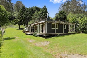 A single-story house with a porch, surrounded by a grassy yard and trees.