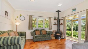 Un salon chaleureux avec une cheminée, deux canapés, un plancher en bois et de grandes fenêtres donnant sur un paysage verdoyant.