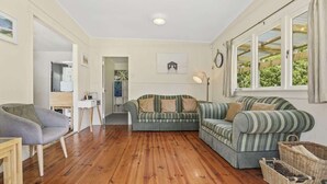 Un salon chaleureux avec un plancher en bois, deux canapés à rayures, un fauteuil gris et une petite table.