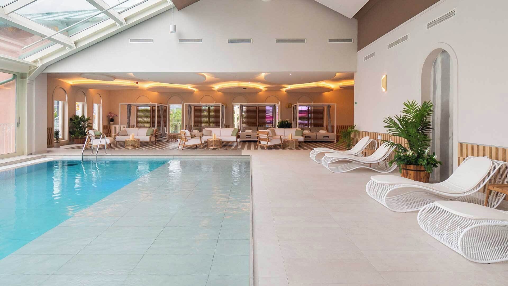 A large indoor swimming pool with lounge chairs and a ceiling with skylights.