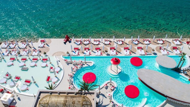 Zona de piscina en un complejo turístico con numerosas tumbonas y una piscina central con detalles circulares rojos.