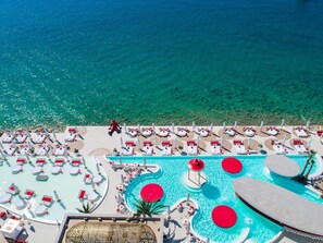 A resort pool area with multiple sun loungers and a central pool with red circular features. - Amadria Park Beach Hotel Niko (Sibenik)