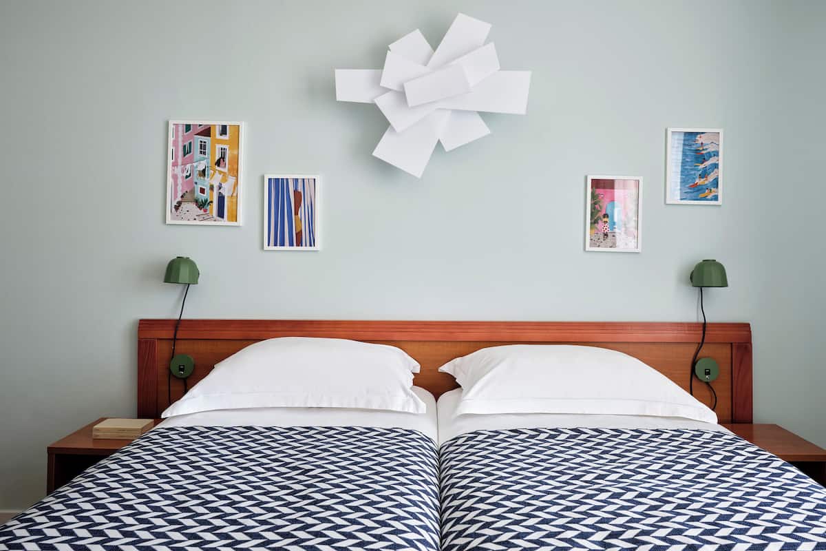 A double bed with a geometric patterned bedspread, a wooden headboard, and a wall with framed artwork.