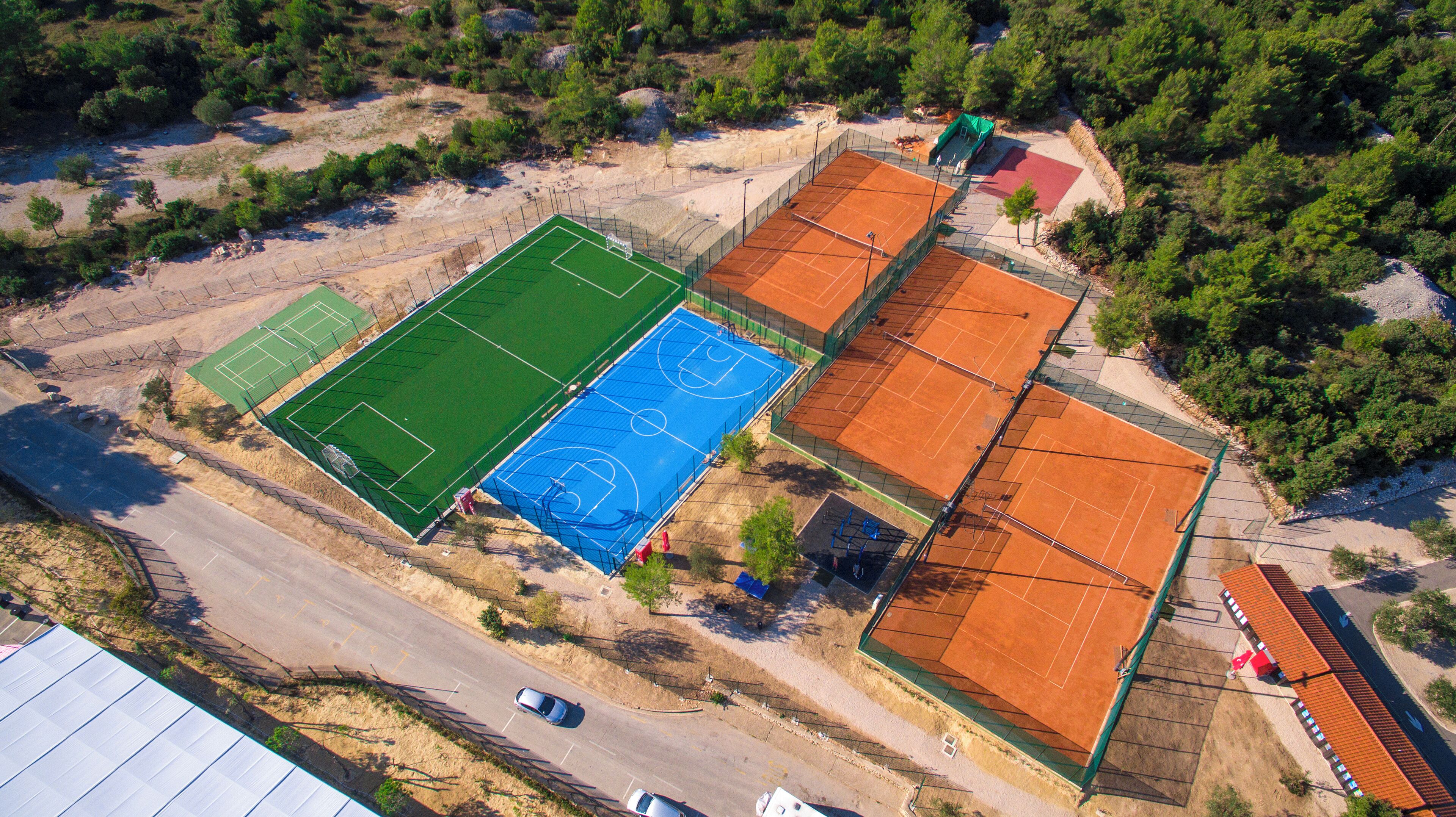 Eine Vogelperspektive auf einen Sportkomplex mit mehreren Tennisplätzen, einem Fußballfeld und einem Parkplatz.