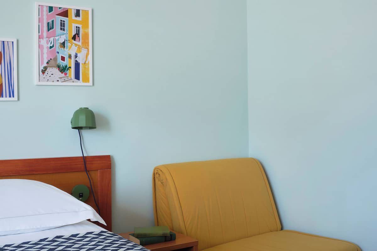 A bedroom with a bed, a chair, a nightstand, a lamp, and two wall art pieces.