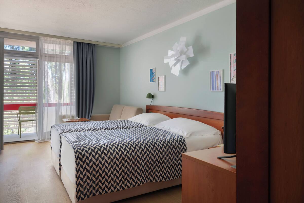 A hotel room with a bed, a desk, a chair, a TV, and a window with curtains.