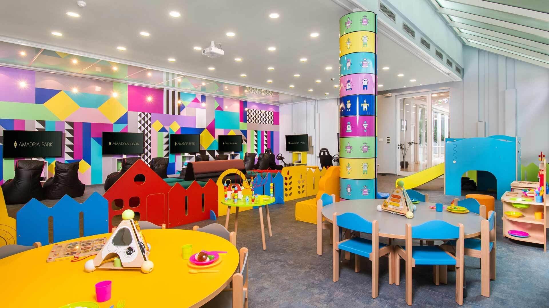 Un área de juegos infantil vibrante con mobiliario colorido y diseños geométricos en las paredes.