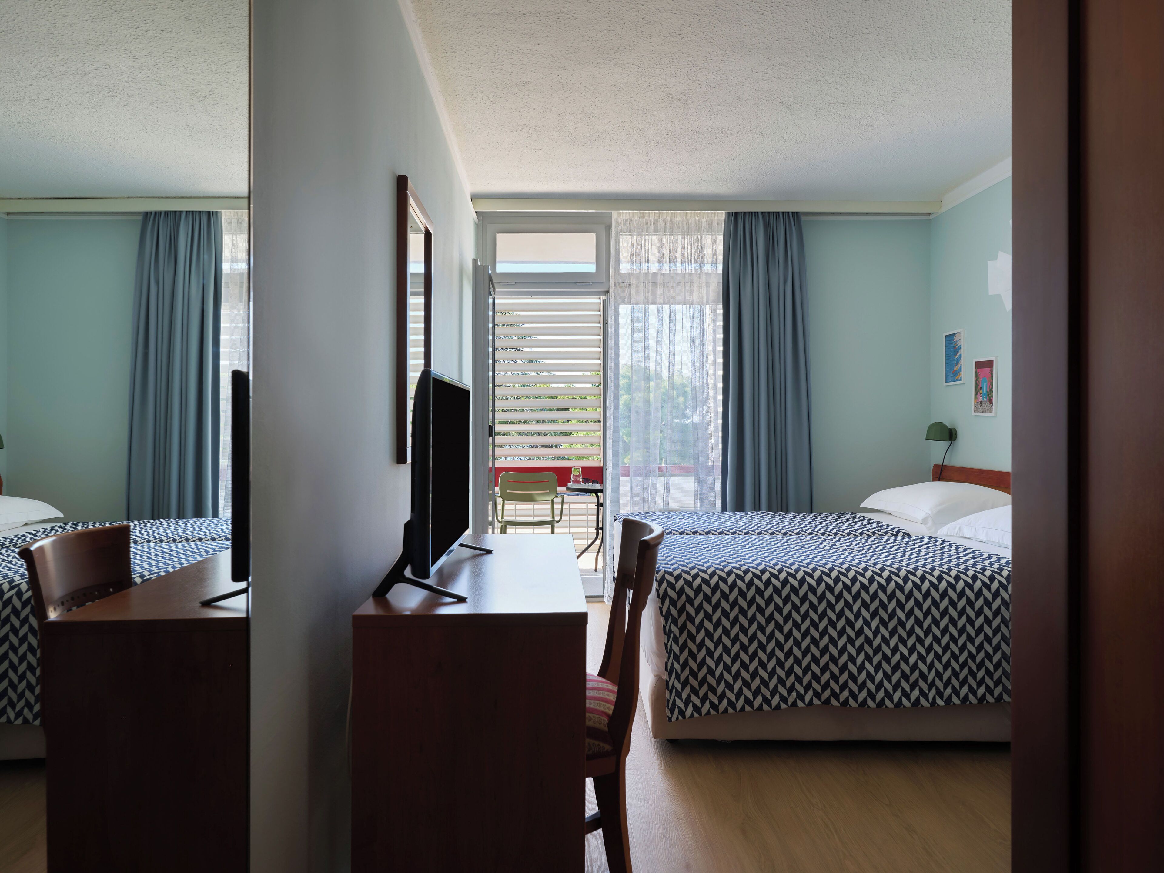Habitación de hotel con dos camas, un escritorio, una silla, un televisor y una ventana con cortinas.