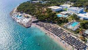 Vista aérea de un complejo turístico costero con múltiples piscinas, zonas de playa con sombrillas y una variedad de edificios.