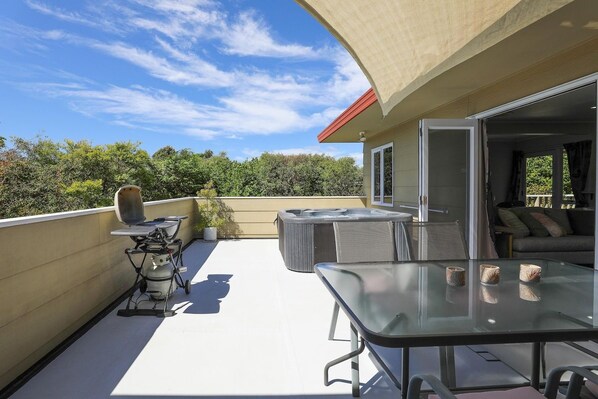 An outdoor patio with a glass table, chairs, a grill, and a hot tub.
