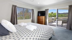 Ein Schlafzimmer mit Bett, Fernseher, Kommode und einem Balkon mit Blick ins Grüne.