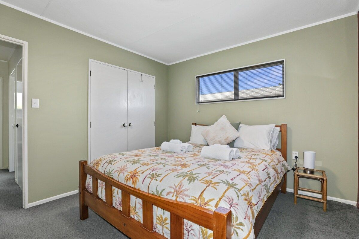 A bedroom with a bed, a window, a door, and a small bedside table.