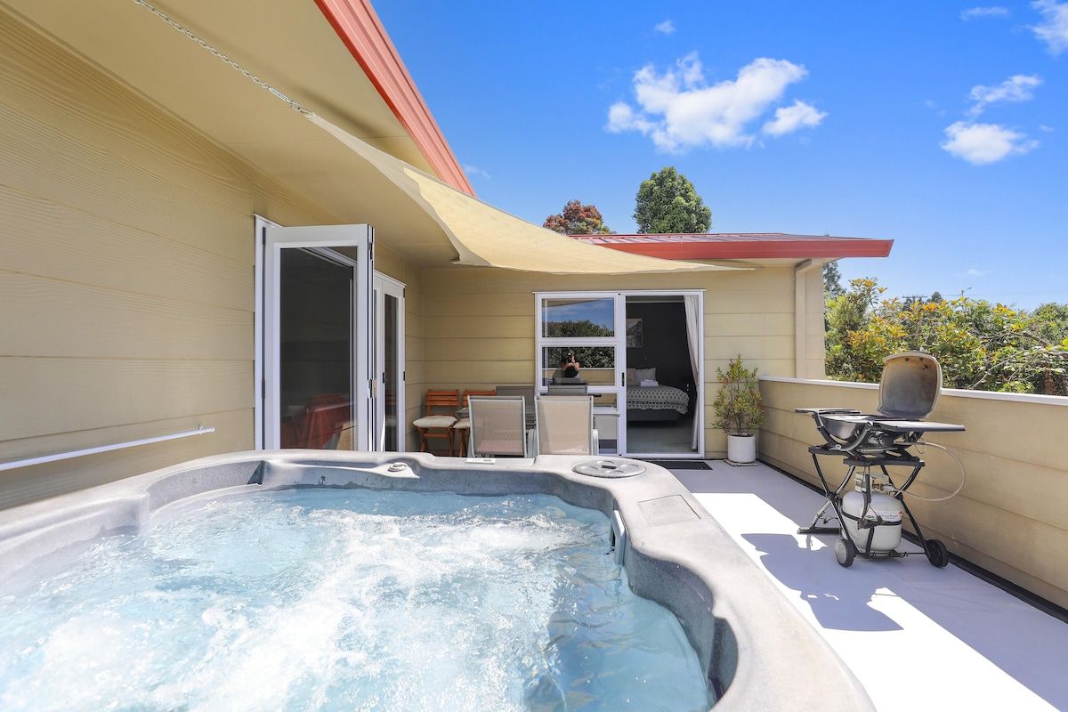 A hot tub on a balcony with a patio area, a sliding door, and a small table with a grill.