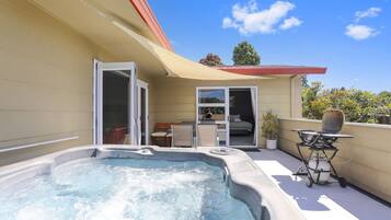Una bañera de hidromasaje en un balcón con zona de patio, una puerta corrediza y una pequeña mesa con una parrilla.