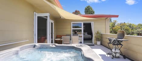 A hot tub on a balcony with a patio area, a sliding door, and a small table with a grill.