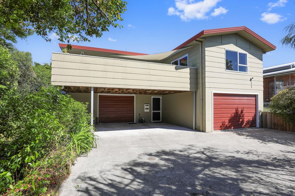 A two-story house with a garage, a covered driveway, and a red roof.