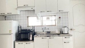 Une cuisine de taille réduite, avec des meubles blancs, un four à micro-ondes, une cuisinière et un évier.