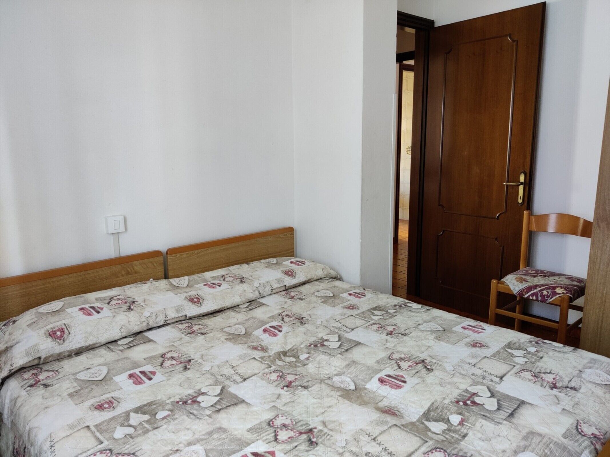A bedroom with a bed, a wooden door, and a chair.