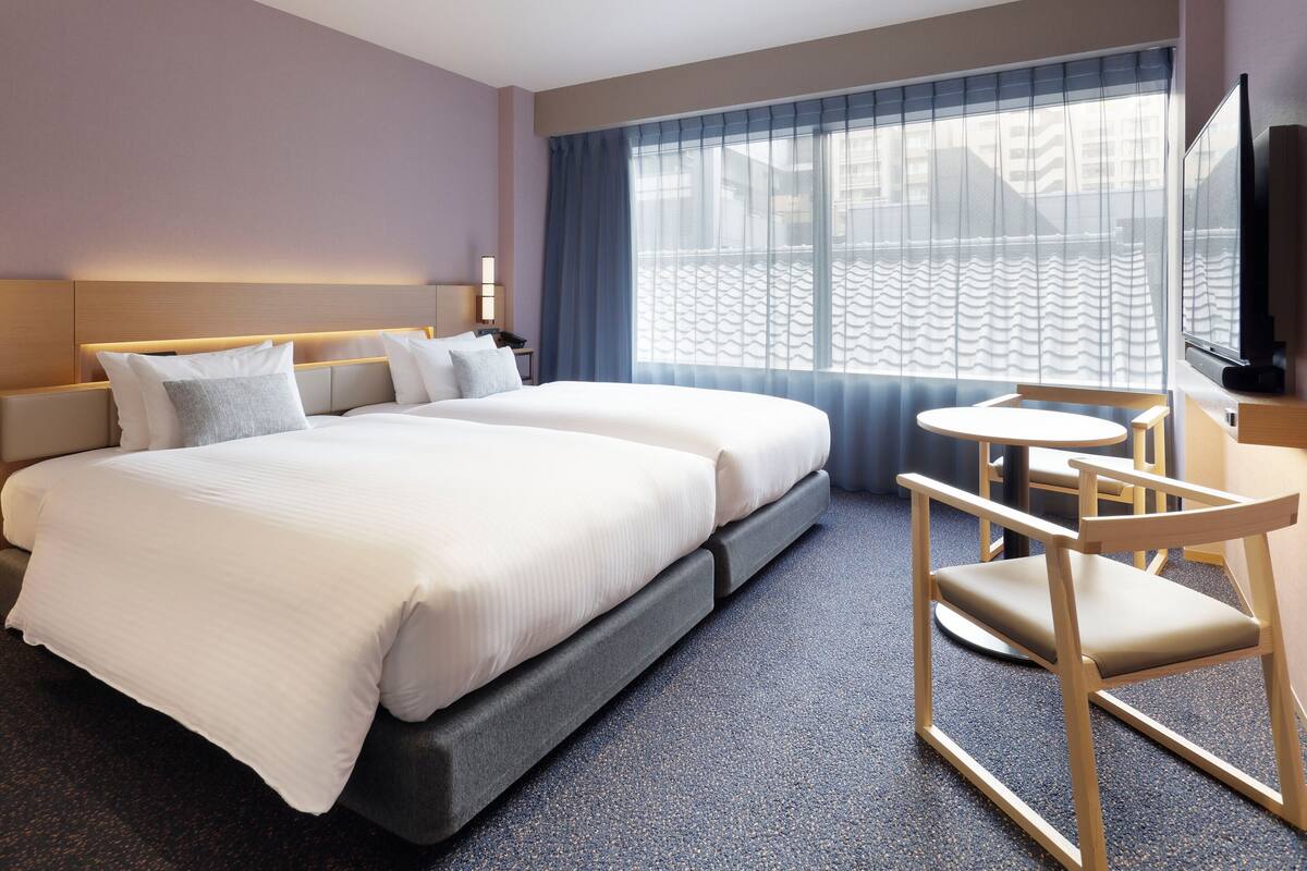 Ett hotellrum med en säng, sängbord, en tv och ett fönster med gardiner.