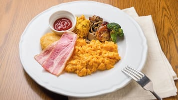 Um prato de comida com ovos mexidos, bacon, purê de batatas e acompanhamento de legumes.
