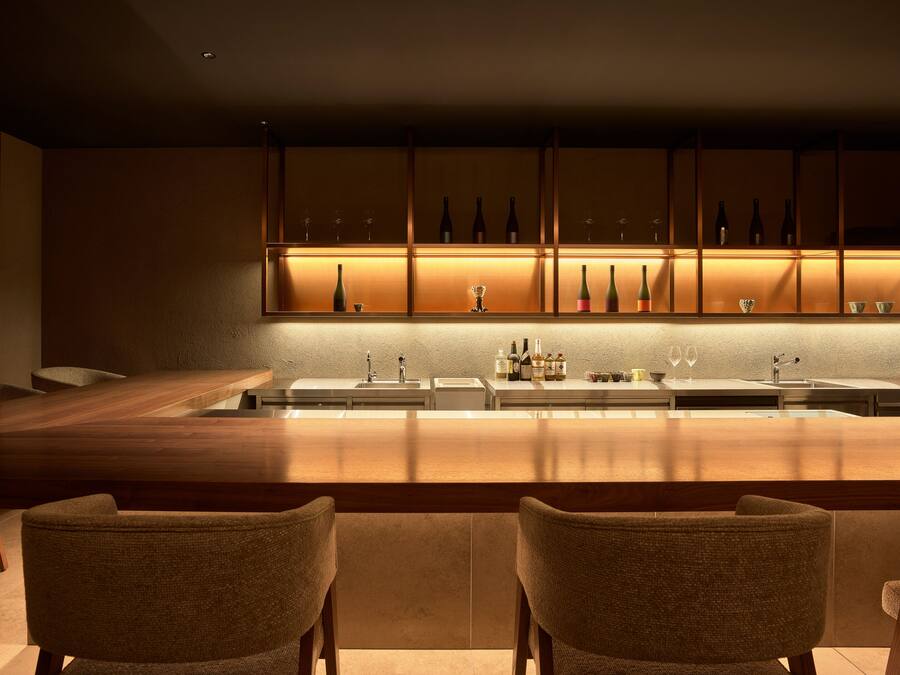A modern kitchen with a central island, two bar stools, and a wine rack with bottles and glasses.