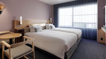 A hotel room with two beds, a small table, a chair, a TV, and a large window with curtains.