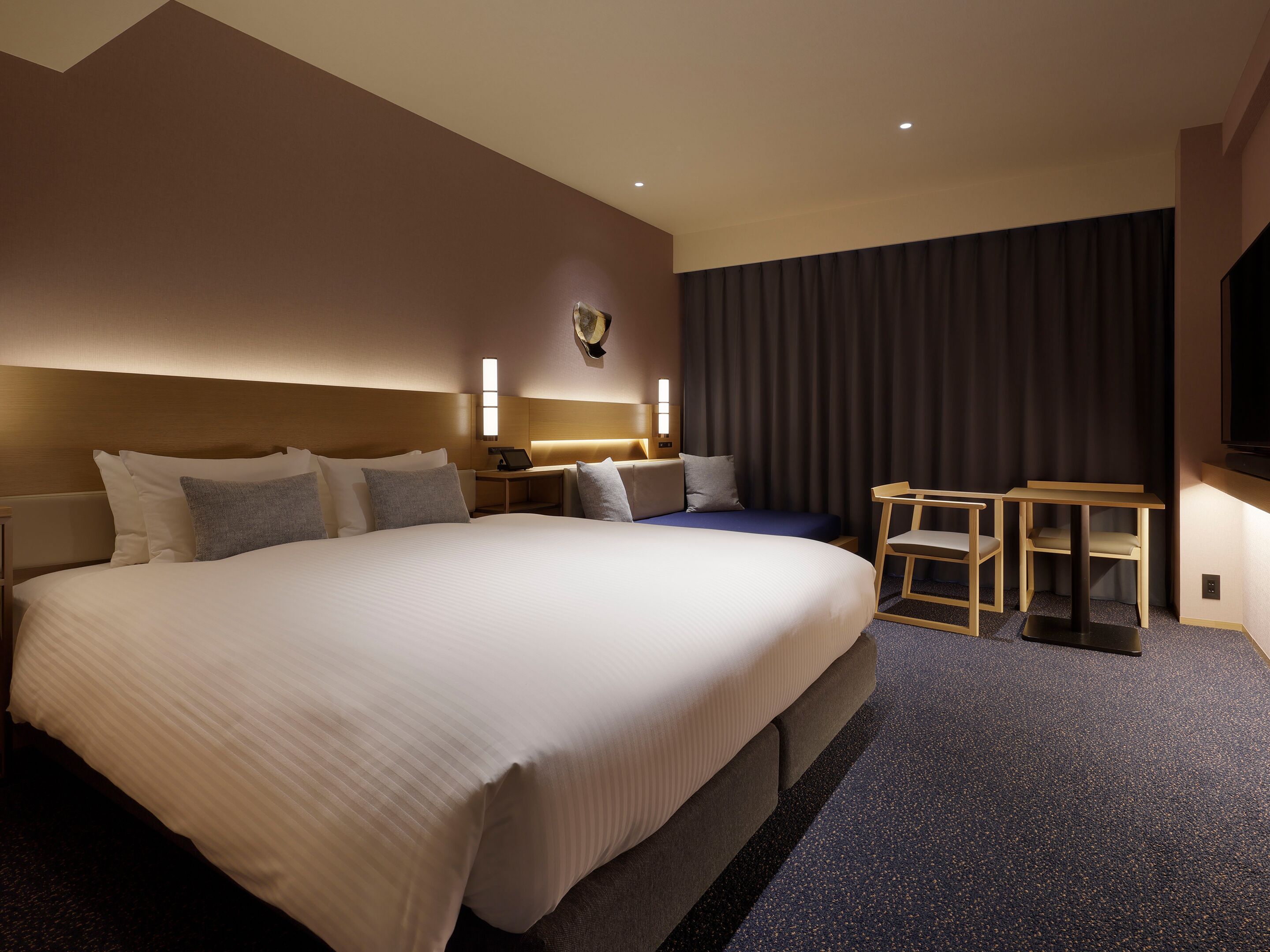 Ett hotellrum med en stor säng, sängbord, ett skrivbord, en stol och en tv.