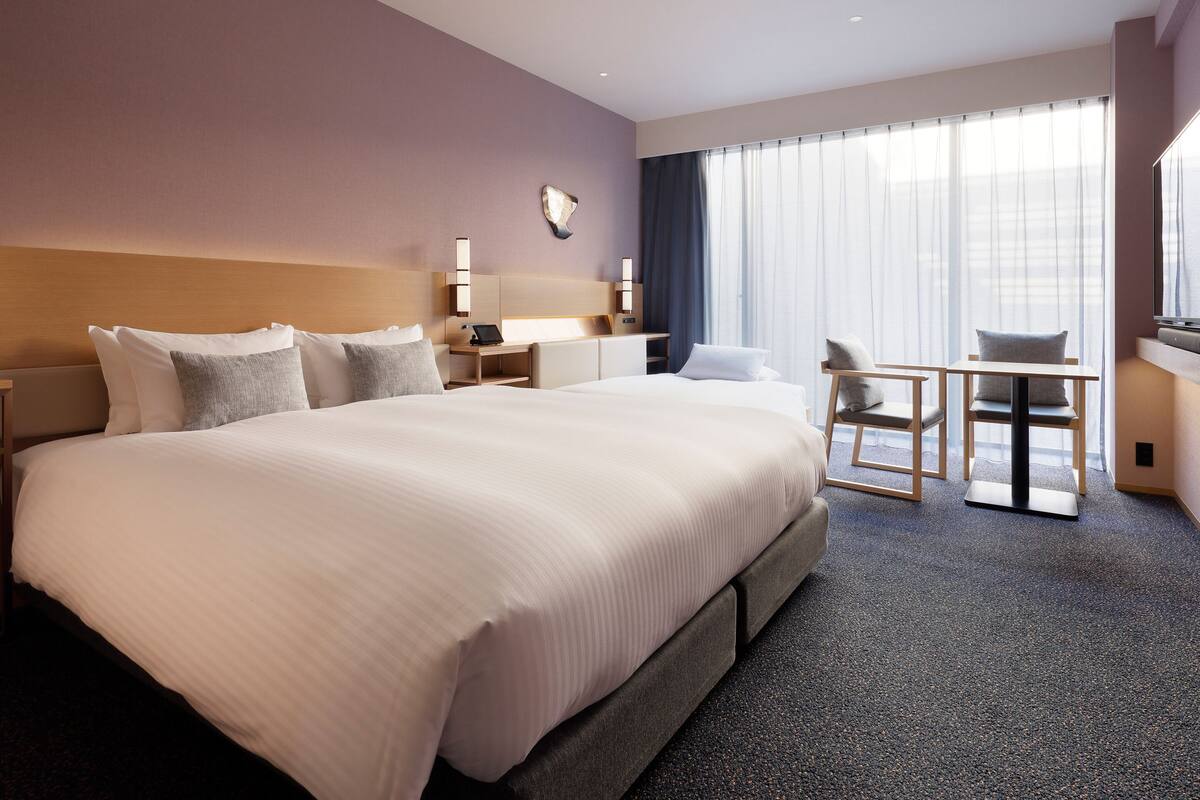 Ett hotellrum med en stor säng, ett skrivbord med en stol, en TV och ett fönster med gardiner.