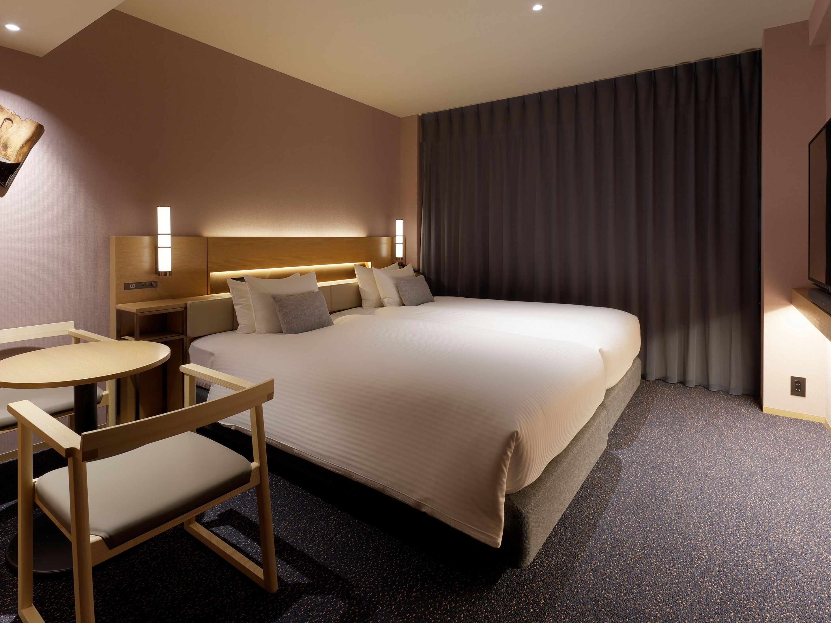 A hotel room with a large bed, a desk with a chair, a TV, and a window with curtains.