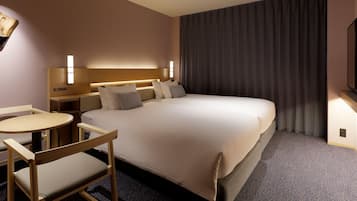 A hotel room with a large bed, a desk with a chair, a TV, and a window with curtains.