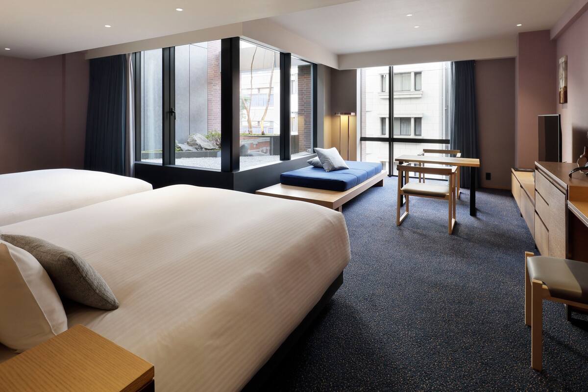 Ett hotellrum med en stor säng, ett skrivbord, en stol och utsikt över staden.