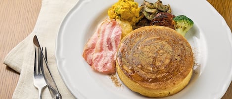 A plate with pancakes, bacon, scrambled eggs, and vegetables on a wooden table.