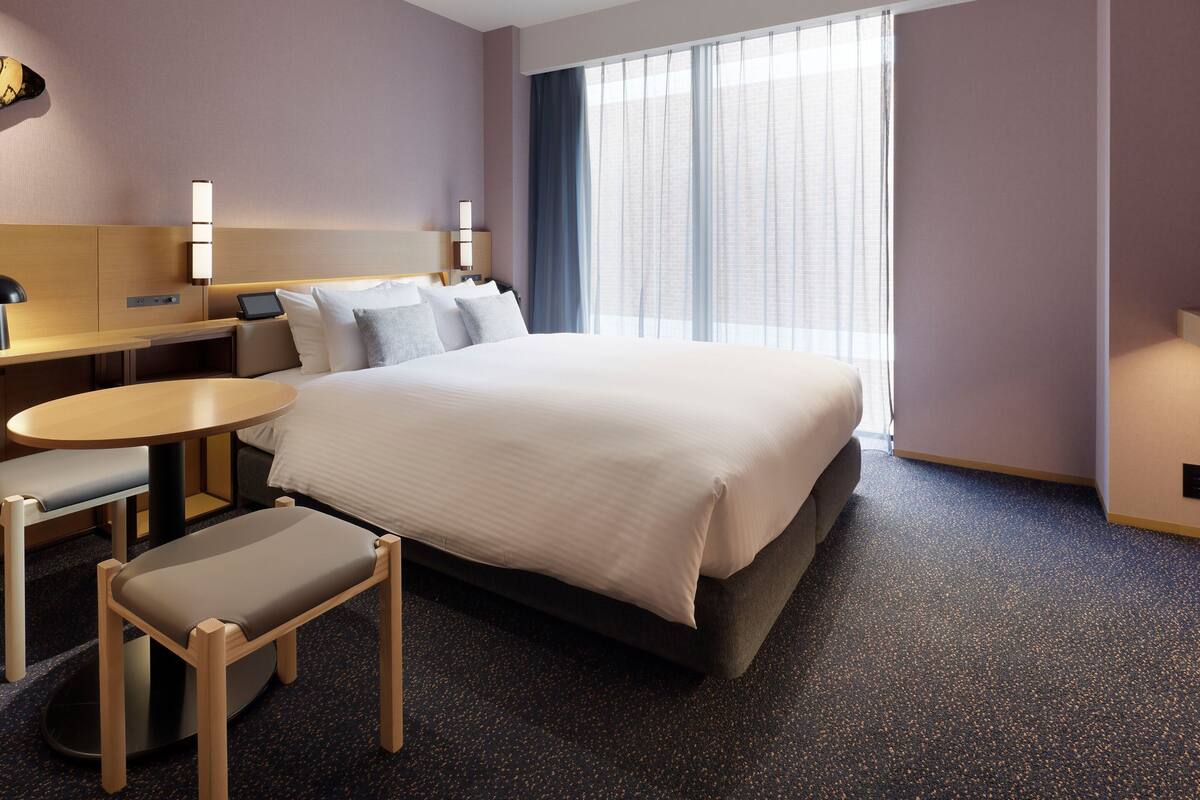 Ett hotellrum med en säng, ett skrivbord, en stol och ett litet bord.