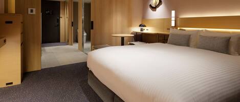 Ein Hotelzimmer mit einem großen Bett, einem Schreibtisch, einem Stuhl, einem kleinen Tisch und einem durchgegangene Tür sichtbaren Badezimmer.