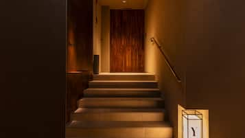 A staircase with a wooden door at the top, a handrail, and a wall-mounted light fixture.