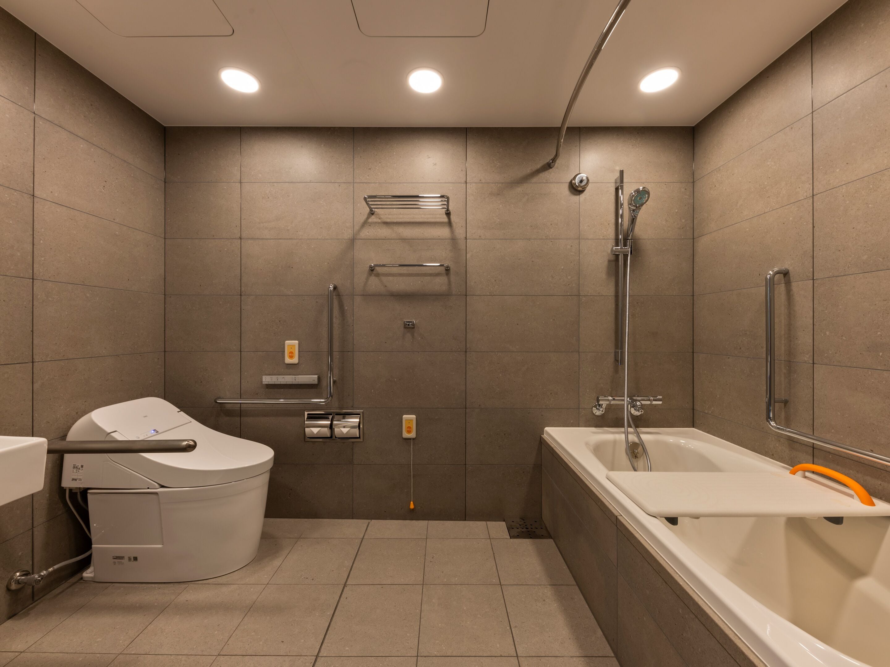 A modern bathroom with a shower, toilet, and bathtub, equipped with grab bars and a hand dryer.