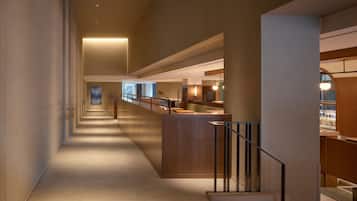 A modern hotel corridor with a long, narrow layout, a reception desk, and a seating area with tables and chairs.