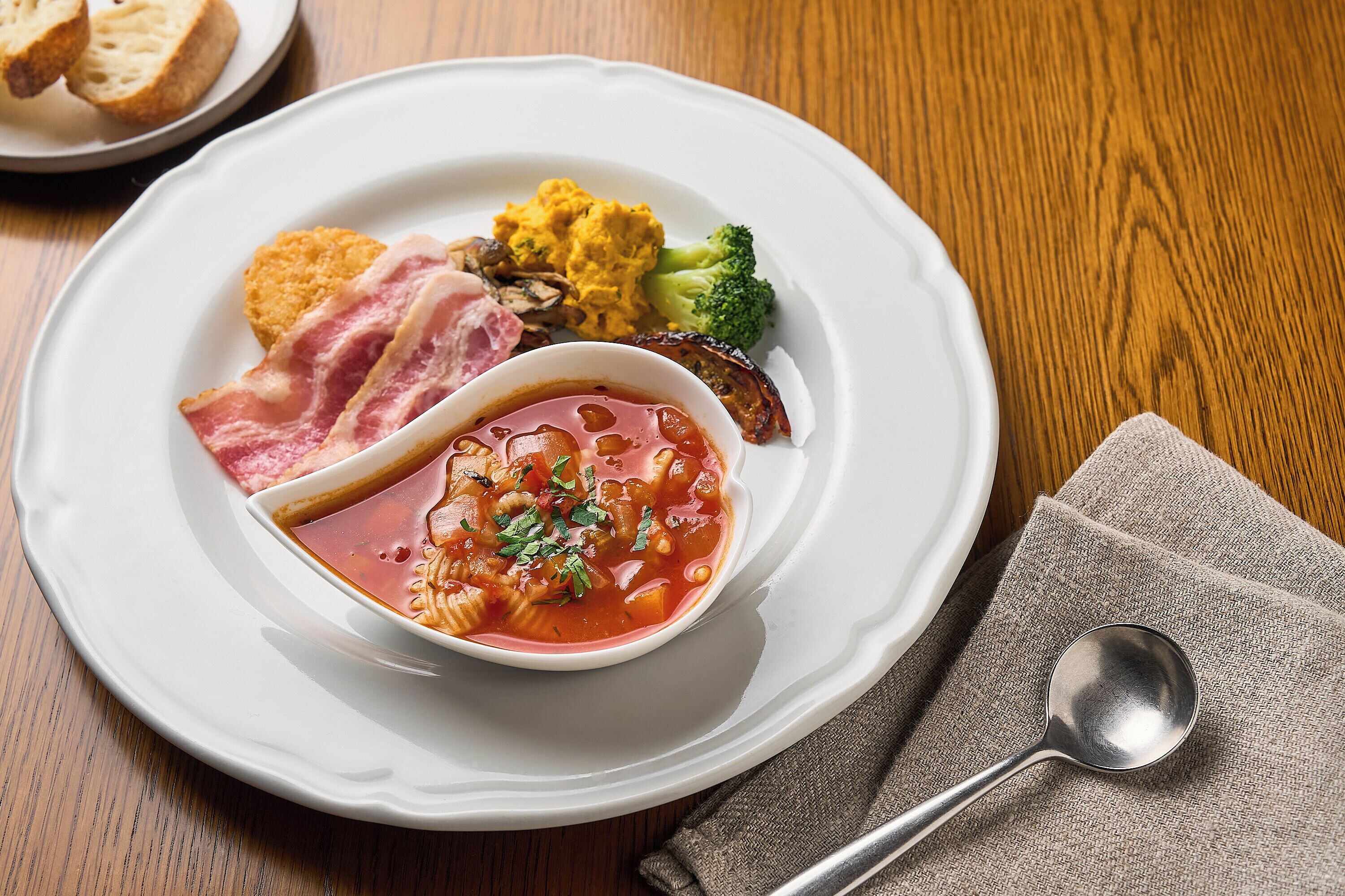 A plate of food with a bowl of soup, broccoli, and bread.