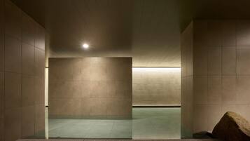 A modern, minimalist bathroom with a large mirror, tiled walls, and a stone accent piece.