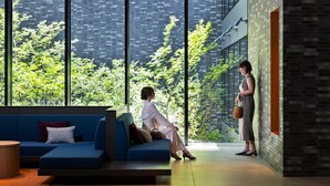A modern interior with a blue sofa, a wooden table, and a large window offering a view of greenery and a brick building. - Mitsui Garden Hotel Kyoto Sanjo PREMIER (Kyoto)