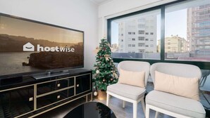 Una sala de estar moderna con un televisor grande que muestra 'hostwise', un árbol de Navidad y dos sillones blancos.